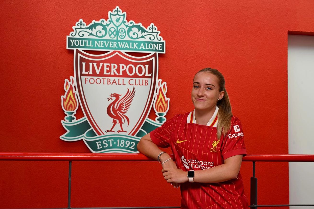 New Liverpool FC Women midfielder Kirsty Maclean leans against a wall in front of the Liverpool crest